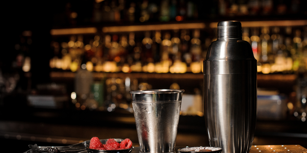 A steel shaker and jigger on a bar